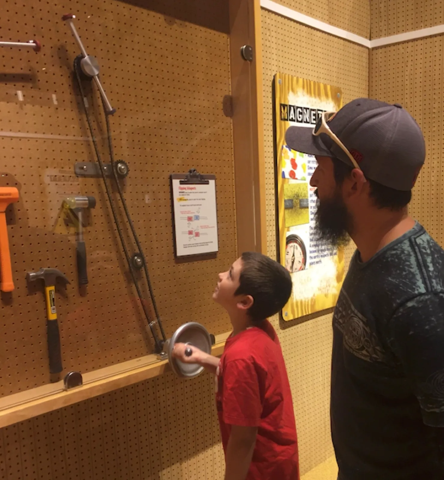 A child and an adult exploring a hands-on tools and pulleys exhibit at a science museum